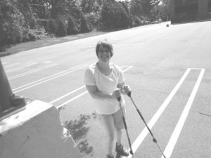 Black-and-white photograph of Kerry Ann Wiley standing with forearm crutches in a parking lot.