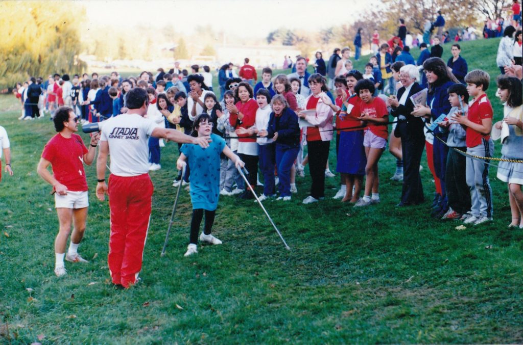 Kerry Ann Wiley walking with forearm crutches in a race as spectators cheer along the course.